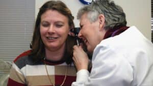 Profesional de salud examina el oído de una paciente con un otoscopio en un consultorio.